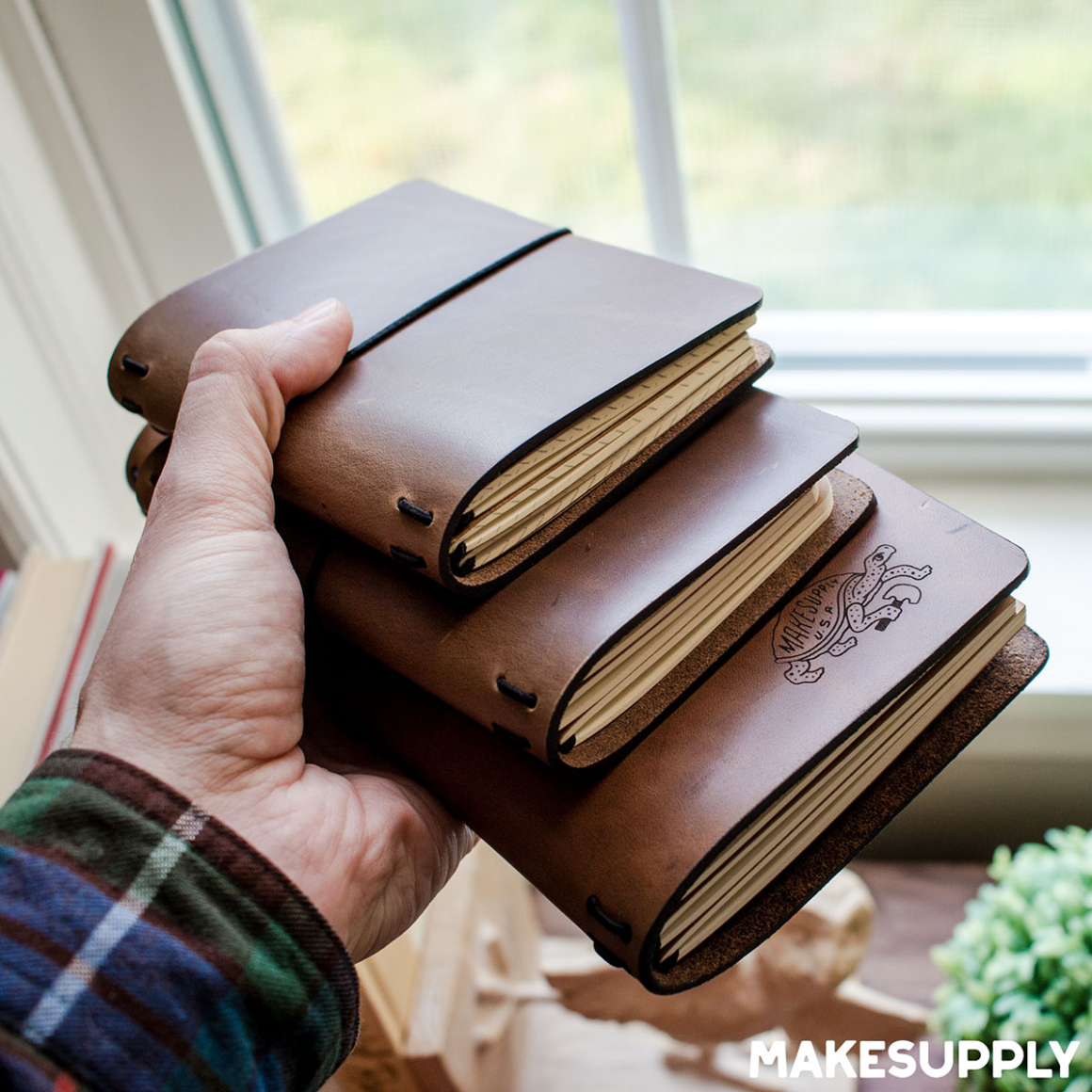 Three finished travel-style leather journal covers stacked together in pocket, passport, and standard traveler sizes