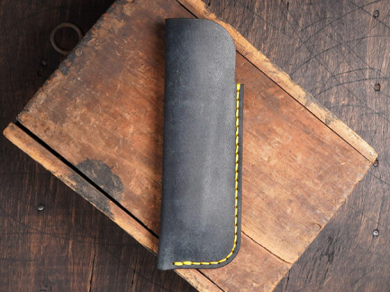 Leather pen sleeve with hand stitched edge on a rustic wood surface
