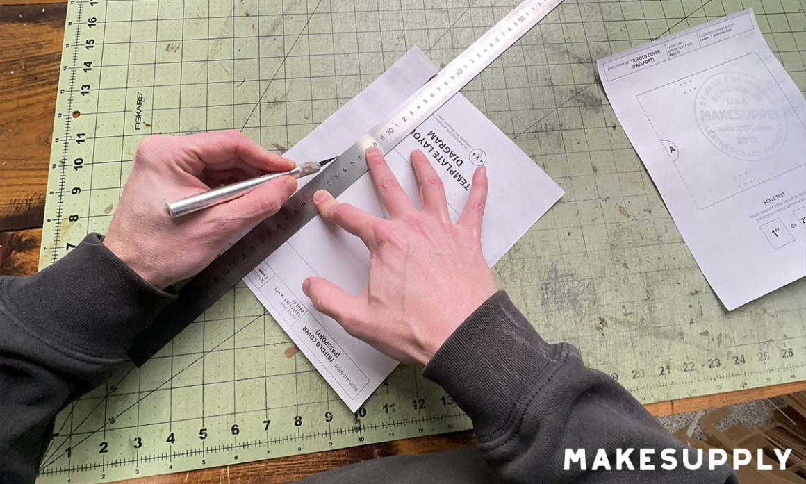 Hands using a metal ruler and craft knife to cut along the dashed line on the first template page.
