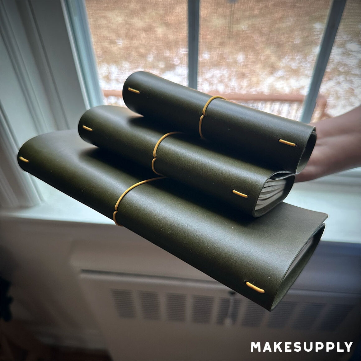 Three tri-fold traveler journal leather covers stacked with elastic bands (standard, pocket, and passport sizes=