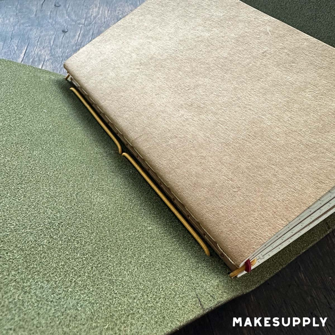 Close-up of a tri-fold leather traveler journal cover holding a removable notebook insert with elastic cord.